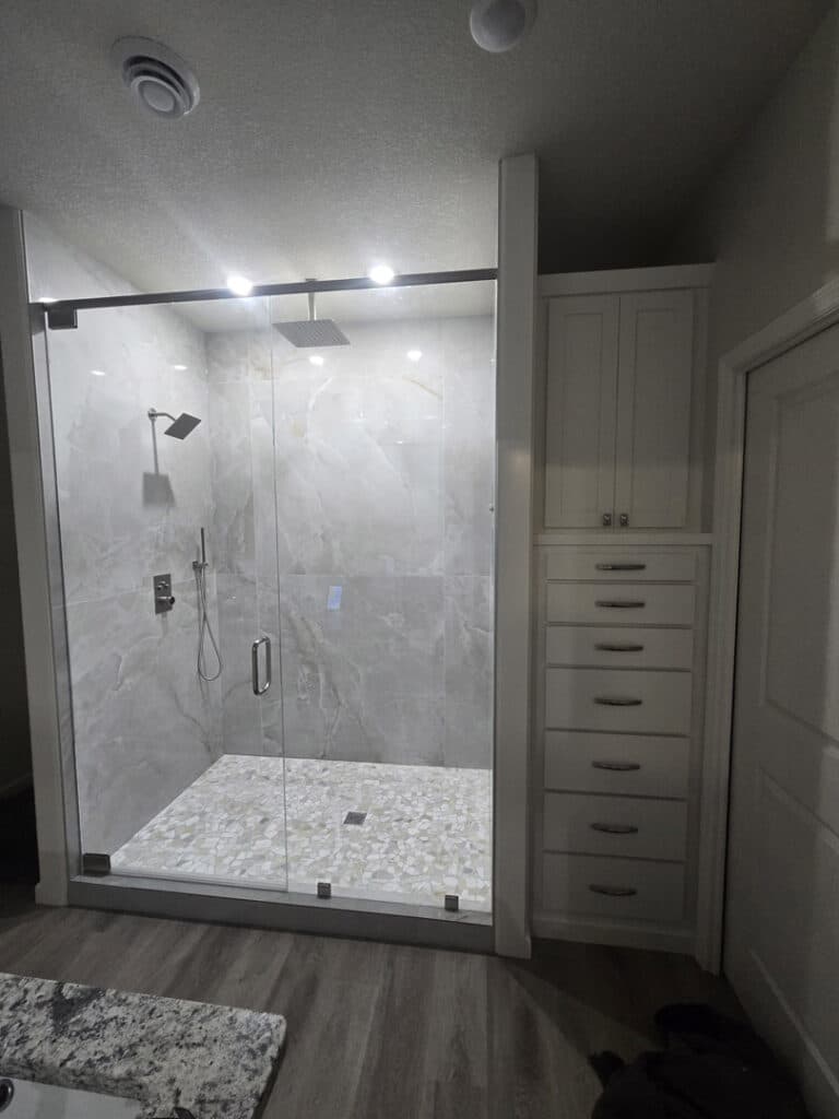 Frameless glass shower enclosure with black hardware, large format tile, and modern bathroom cabinetry