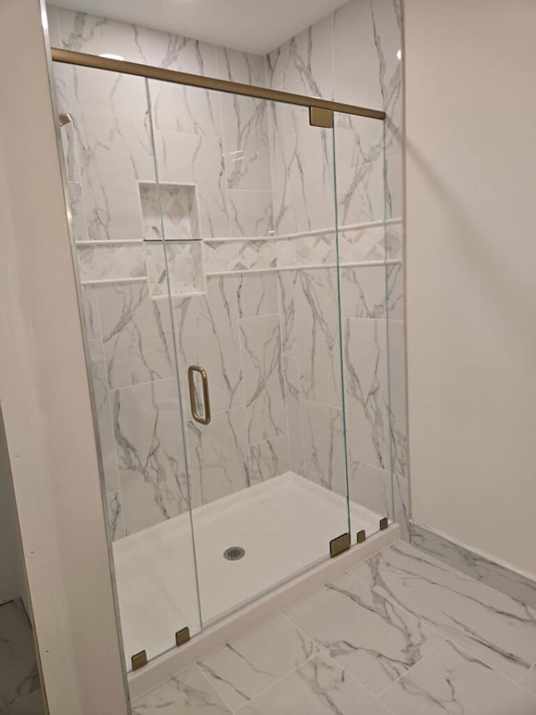 Sliding glass shower doors with brass hardware and marble tile surround