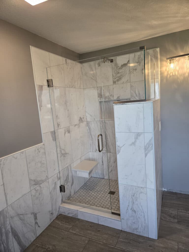 Custom frameless glass shower with hinged door, marble tile surround, and built-in bench