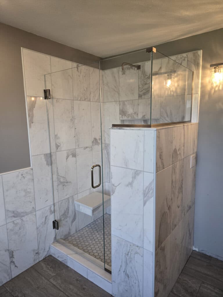Angled frameless glass shower enclosure with bronze hardware and marble tile walls