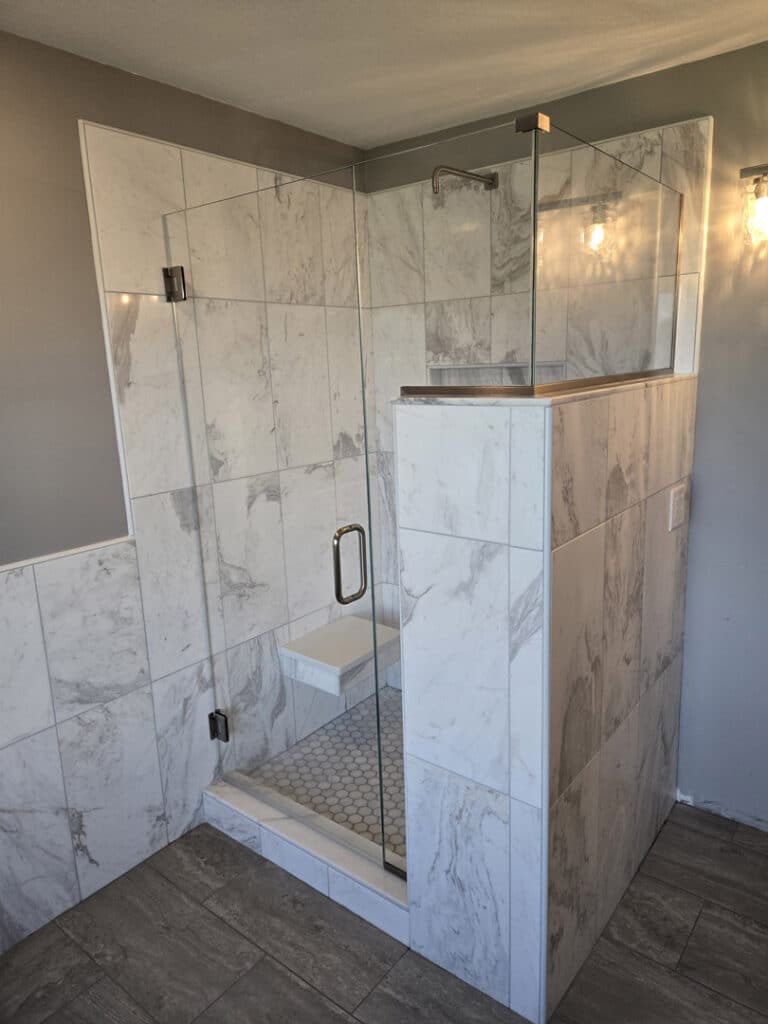 Corner frameless glass shower with custom knee wall, marble tile, and modern hardware