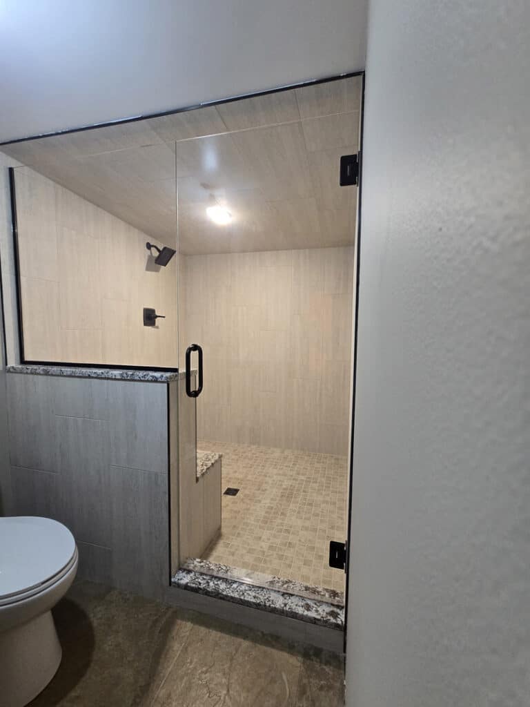 Frameless glass shower with black hardware, tiled bench, and walk-in design
