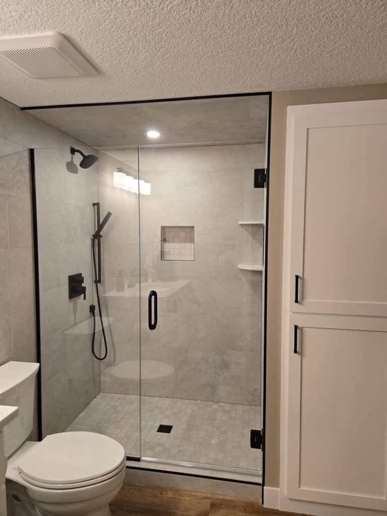 Corner frameless glass shower with black hardware, built-in niche, and light gray tile
