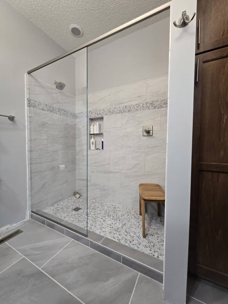 Frameless glass walk-in shower with tile surround, built-in niche, and pebble tile floor