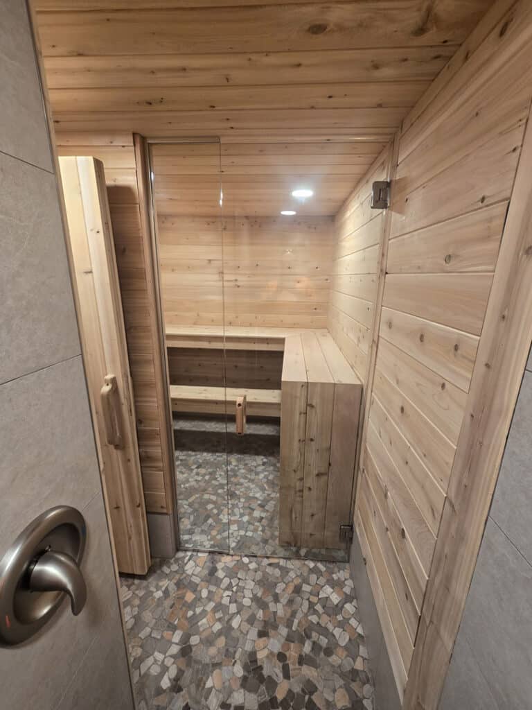 Custom glass sauna door with cedar interior, built-in bench, and stone tile flooring