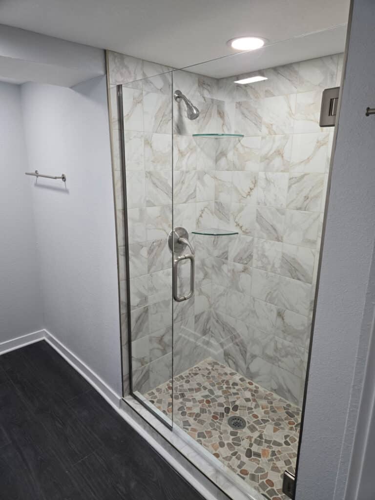 Frameless glass shower enclosure with stone tile floor and floating glass shelves