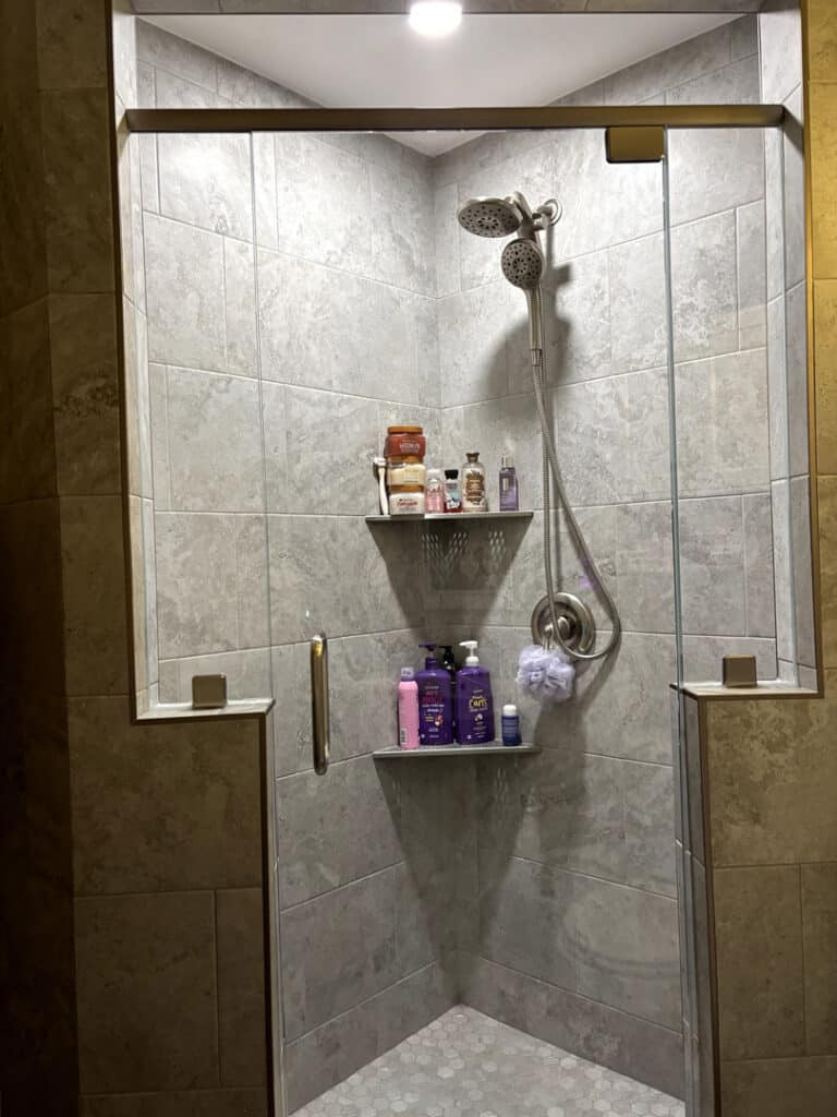 Sliding glass shower door with bronze hardware and tiled shower with corner shelving